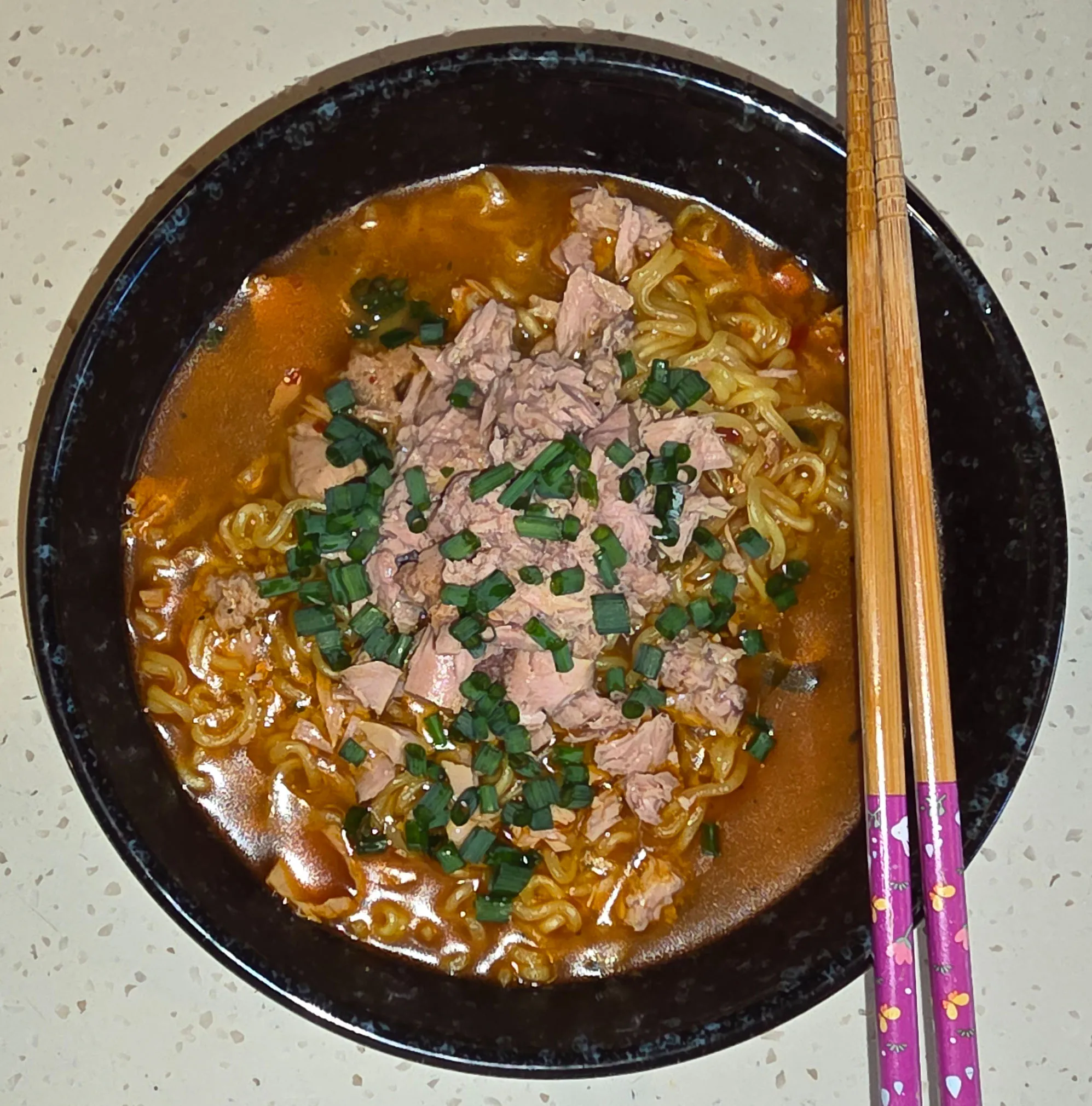 A ceramic boul of shin ramyun with a can of tuna chunk, and chopped scallions